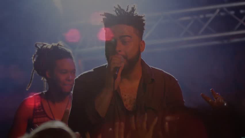 Male singer stepping into spotlight on stage engaging fans with red hex lights drifting overhead. Performance, musician, concert, stage, entertainment, spotlight, music
