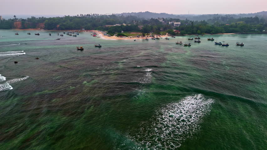 Aerial view of fishing boats anchored near Weligama Fisherman’s Village Beach, Sri Lanka, with turquoise water and a calm tropical shoreline.