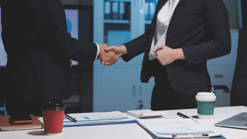 Two women are looking at a table with many papers and graphs. One of the women is holding a pen