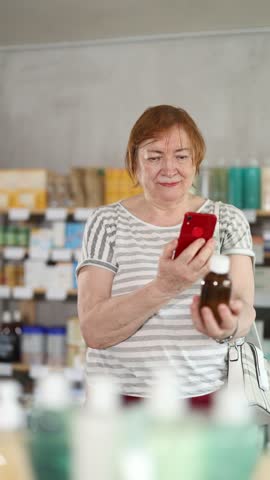 Near display case in pharmacy, senior woman scans barcode on antitussive syrup. Client collects customer information online, seek reviews and recommendations for use