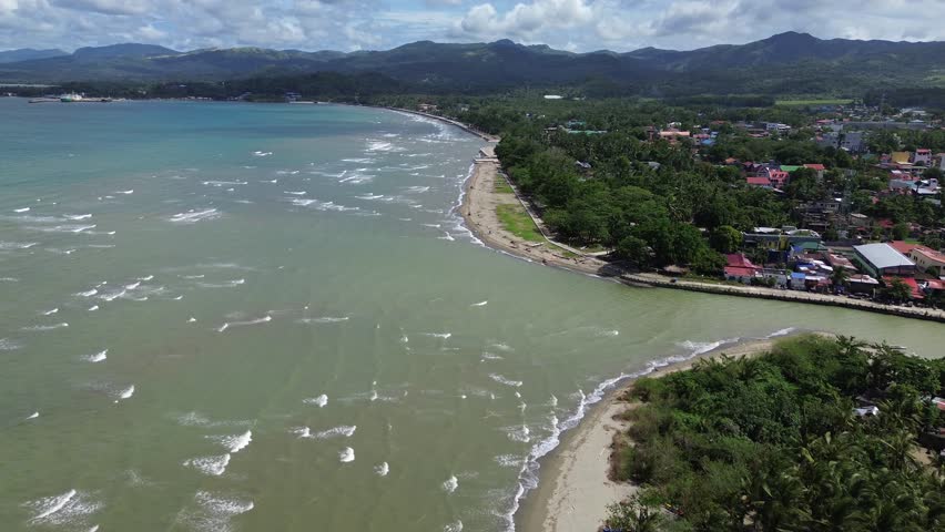 Aerial drone footage of a river flowing into the sea in Odiongan, Philippines, surrounded by dense green forest, palm trees, sandy shoreline and rolling hills and Mountains in Background, sunny day.