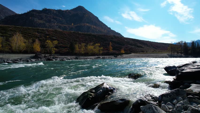 Rushing Rapids In Foreground With Alpine Peak And Sunlit Trees, CloseUp River Flow Over Rocks Creates Dramatic Whitewater, Shimmering Reflections And Splashing Droplets, Rugged Shoreline And Distant