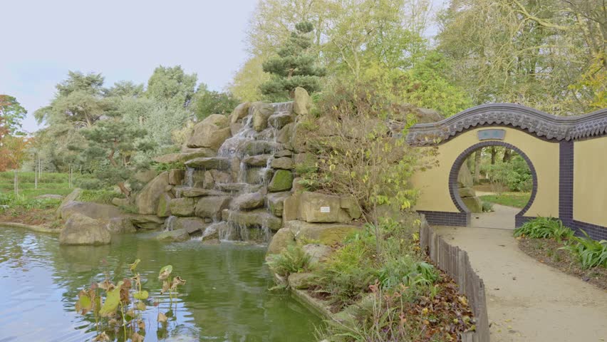 A serene Chinese garden in Parc de Maurepas, featuring a rock waterfall, tranquil pond, and traditional moon gate. Ideal for travel, cultural, and relaxation concepts, Rennes in France