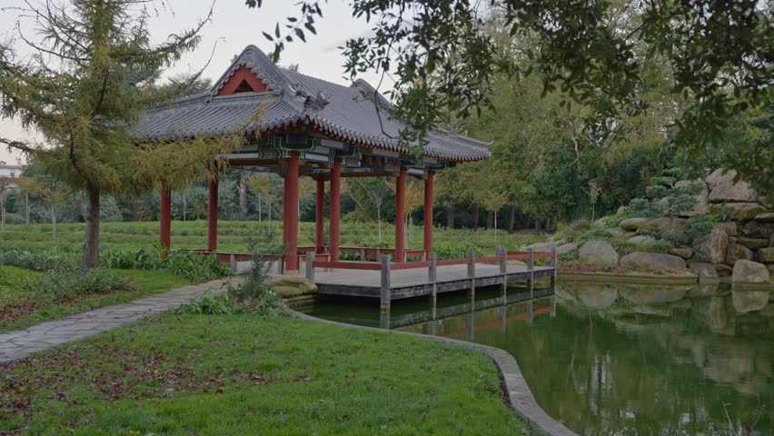 A serene Chinese garden in Parc de Maurepas, featuring a traditional pagoda and its reflection in a tranquil pond. Ideal for travel, cultural, and relaxation concepts, Rennes in France
