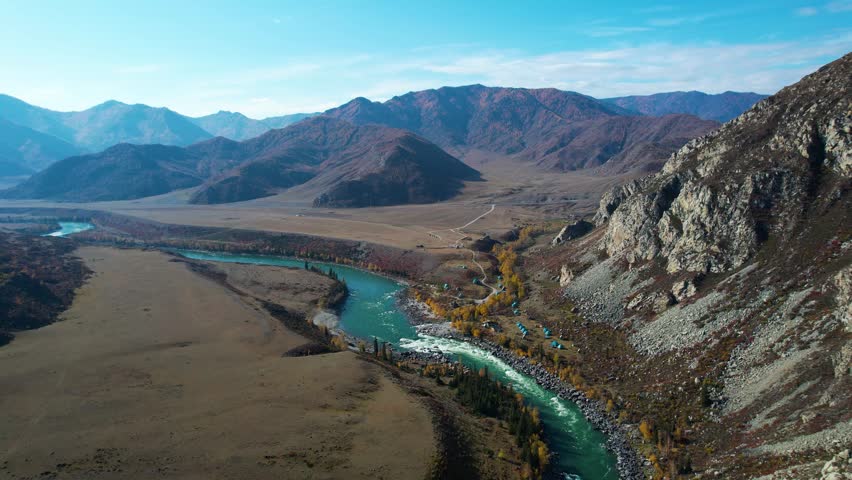 Aerial Turquoise River Winding Through Mountains, Late Autumn Steppe Valley With Rocky Cliffs, Clear Skyscape And Distant Peaks Drone Glides Along Meandering Stream Revealing Pristine Wilderness,