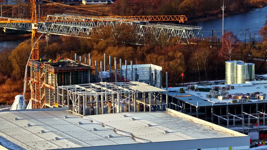 Aerial drone reveals large data center construction site with steel frames, cranes, and active industrial work, early morning sun illumination, establish