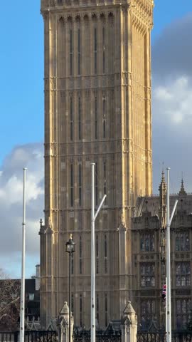 Iconic elizabeth tower, commonly known as big ben, tilting upwards revealing the clock face and spire against a blue sky with clouds in london