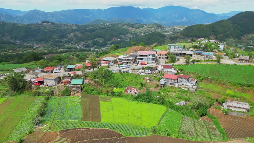 Overhead circling aerial of vibrant green rice terraces and rural mountain settlements along a winding road in Amganad, Ifugao, Philippines.
