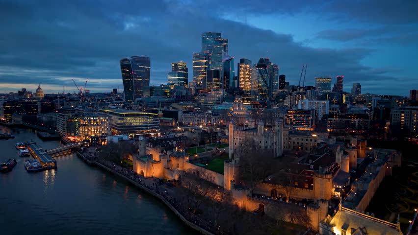 Panoramic aerial view of the illuminated Tower and Tower Bridge in front of the city skyline of London, England, during twilight