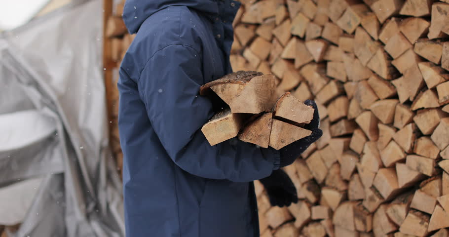 Man collects firewood from stack outdoors in winter. Weather concept.