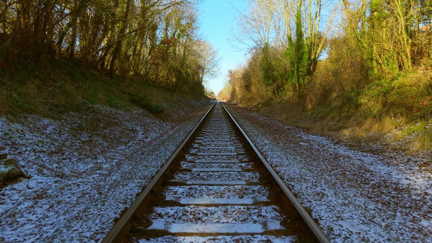 Forward motion along railway tracks through forest corridor while train traveling straight ahead first person view. Direct perspective moving on rails across winter landscape with trees lining route