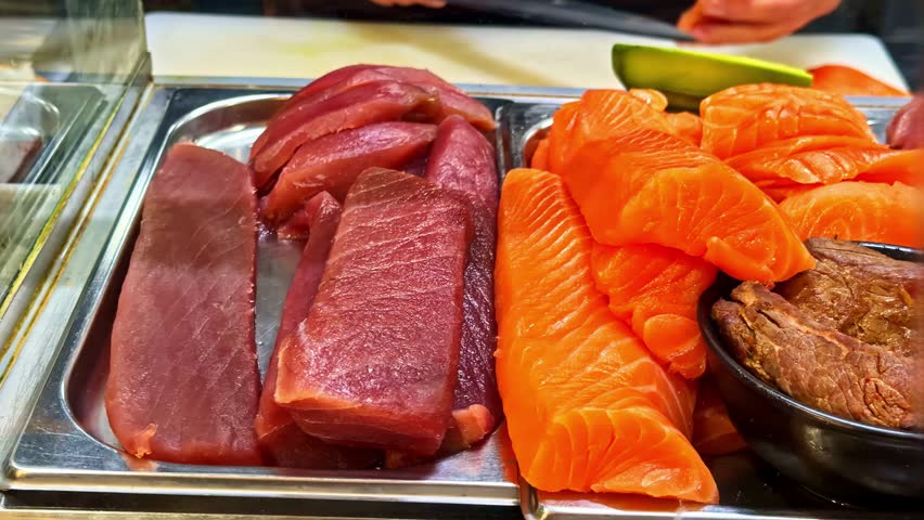 Chef slices fresh salmon, tuna and white fish for sushi and sashimi with avocado on a cutting board, close-up raw seafood prep in a restaurant kitchen.