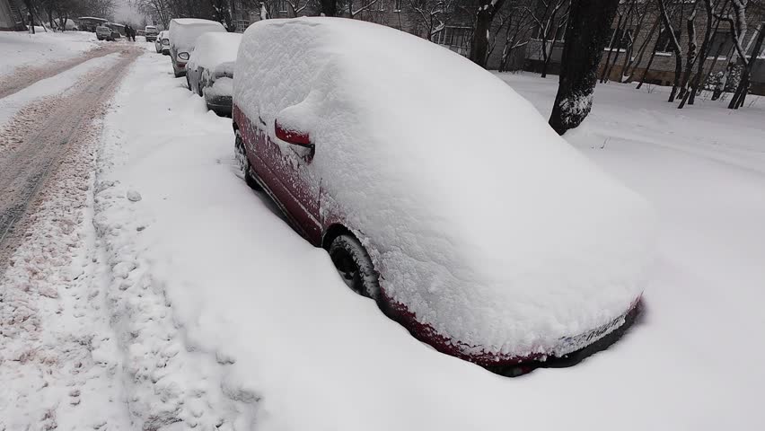 Cars covered in deep snow after a winter blizzard. Vehicles stuck on a city street during heavy snowfall.