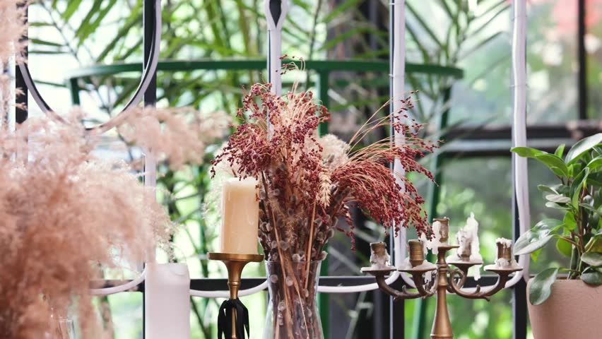Dried millet grass and plumes with candle holders against green foliage backdrop