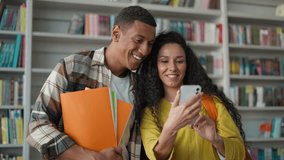 Two people students African American man Indian Hispanic woman use mobile phone smartphone social media online laughing girl guy in library university high school classmates have fun friends studying - Powered by Shutterstock - Get 15% off with code: PIKWIZARD15