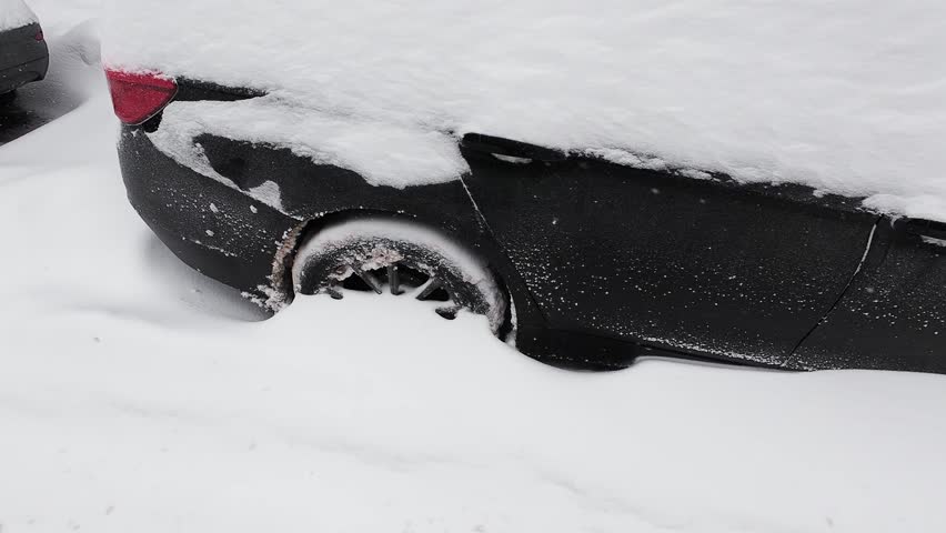 Cars covered in deep snow after a winter blizzard. Vehicles stuck on a city street during heavy snowfall.