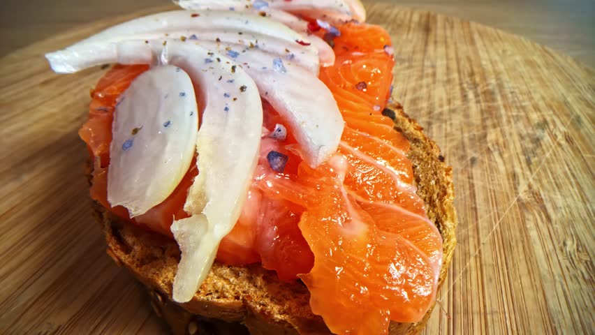 Slow panning macro of raw salmon and sliced onion on bread with salt crystals