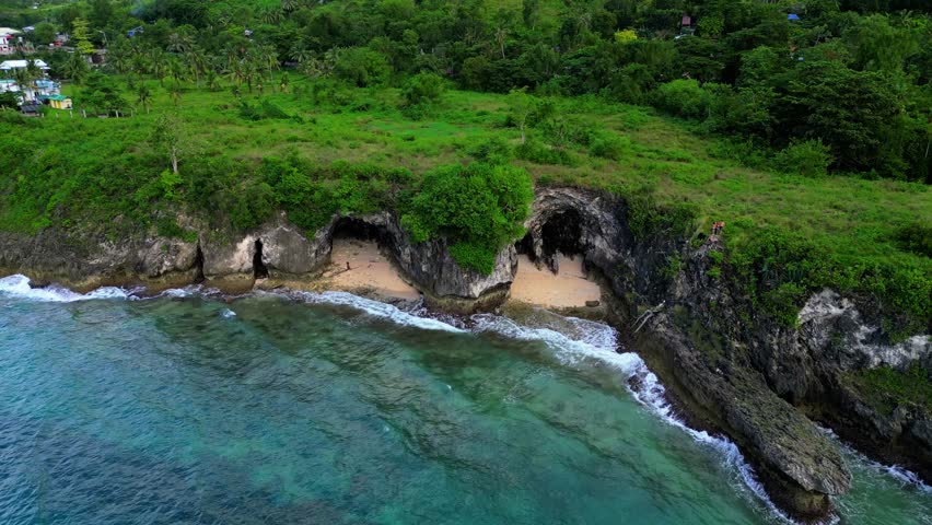 Stunning coastal landscape captured by drone, showing secluded caves, lush greenery, and clear ocean waters under dramatic cloudy skies