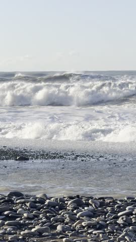 Stormy Waves Crash over Smooth Pebbles on Windy Coastal Shoreline