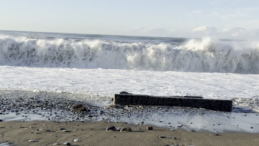 Stormy Waves Crash over Smooth Pebbles on Windy Coastal Shoreline