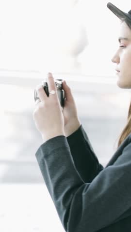 profile view young female photographer with  vintage camera stands near window  adjusts the camera looking at camera Viewfinder, then takes a picture, looks with serious concentration and without a smile. vertical video footage 9:16 