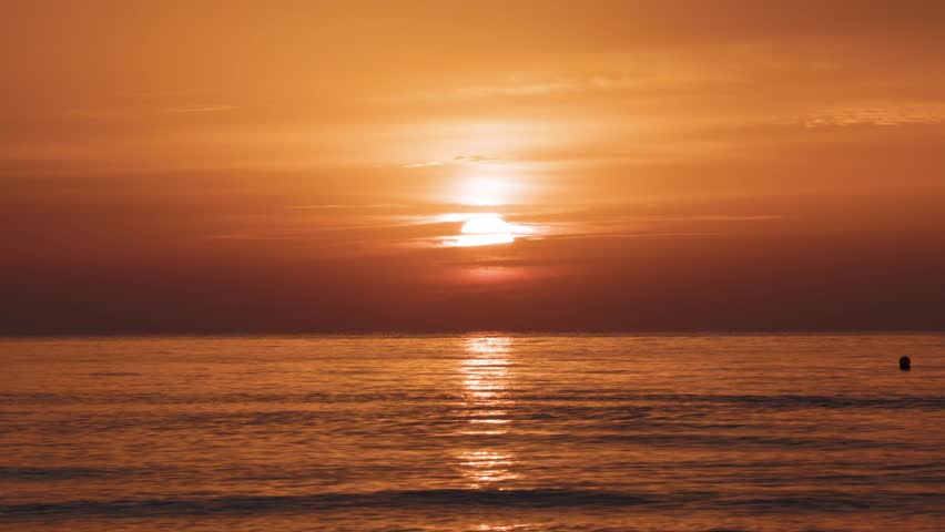 Silhouette of a person swimming alone in open water at dawn, surrounded by warm sunrise tones and gentle waves on the Mediterranean coast
