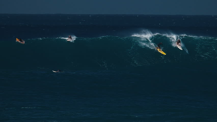 Big wave surfing in Hawaii on Waimea Bay. People surf the huge ocean wave breaking on the Hawaiian shore in Waimea Bay. Surfers share the wave in Hawaii. Oahu island