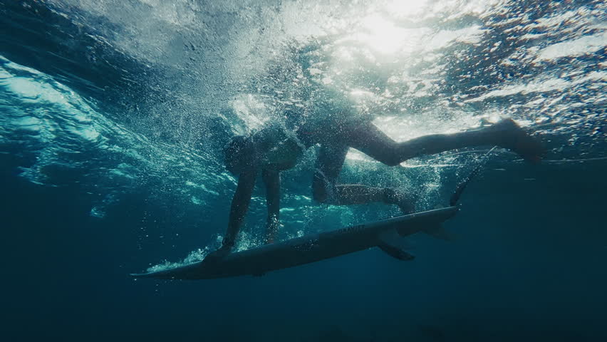 Woman surfer in bikini dives under the ocean wave with surfing board and passes it. Underwater view of the surfer doing duck dive trick