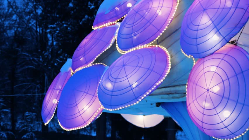 Illuminated lanterns in the shape of a jellyfish in a winter park setting. Soft pink and white lights create a magical, festive atmosphere among the snow.