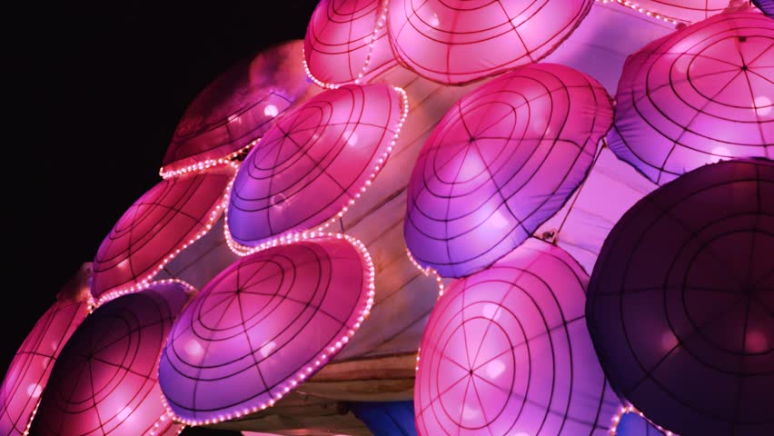 Illuminated lanterns in the shape of a jellyfish in a winter park setting. Soft pink and white lights create a magical, festive atmosphere among the snow.