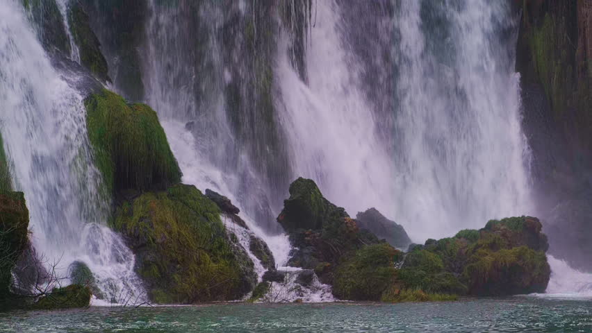 Powerful cascading waterfalls crashing over moss-covered rocks into a turquoise pool below. Kravica Waterfalls, Bosnia and Herzegovina