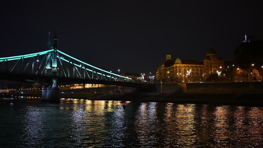 Illuminated Liberty Bridge crossing the Danube River at night with historic city architecture in Budapest, Hungary