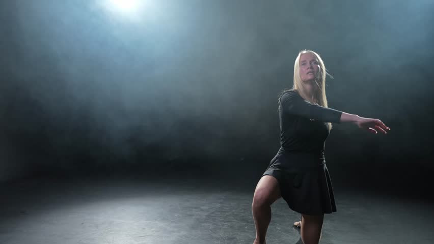 Contemporary woman dancer posing on black background with smoke. Adult female artist performer dancing with expression. Modern ballerina dancing in darkness. Passion dance in dark. Flexibility balance
