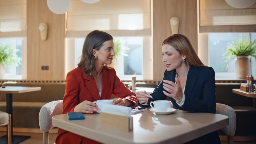 Two colleagues meeting cafe enjoying friendly communication closeup. Smiling elegant woman showing smartphone screen to coworker sitting table together. Couple friends discussing cellphone photo.