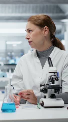 Vertical video Team of laboratory researchers evaluating pharmaceutical compound in petri dish. Female experts in lab brainstorming new drug solutions while inspecting cell culture growth, camera B