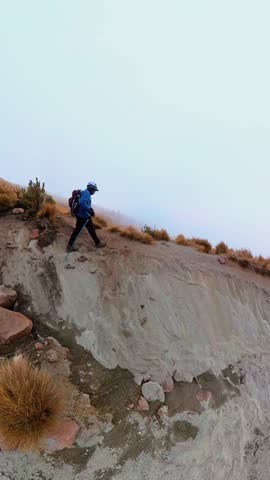Hiker with poles carefully walking down a steep, sandy mountain trail on a foggy day