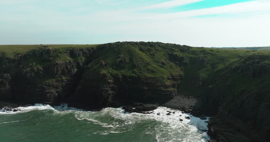 Drone shot pushing in on the East London bluff cliff revealing rugged coastal beauty as waves crash against the dramatic ocean edge