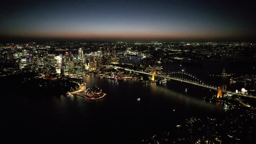 Drone high-angle aerial footage showing the illuminated Sydney Harbour Bridge and the glowing city skyline of North Sydney