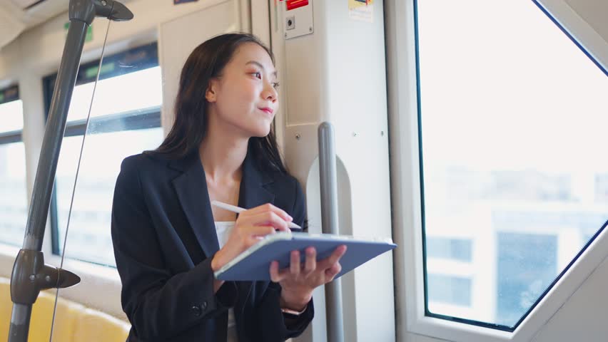 Asian young businesswoman standing on subway train while going to work. Attractive female employee worker feel happy and relax, using digital tablet device with cheerful smile in public transportation