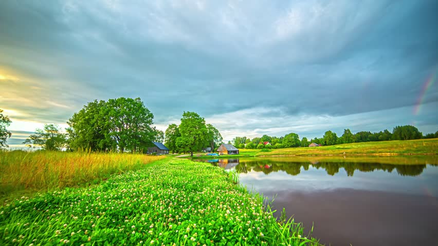 Time lapse of dramatic clouds moving over peaceful countryside pond at twilight
