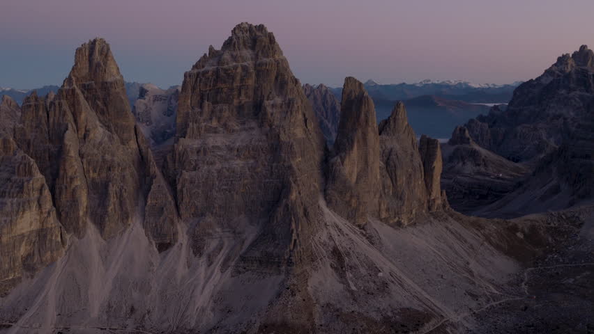 Cinematic aerial view of the Dolomites in Italy, rugged alpine peaks glowing at dawn, dramatic cliffs and deep shadowed valleys creating a serene high-altitude mood