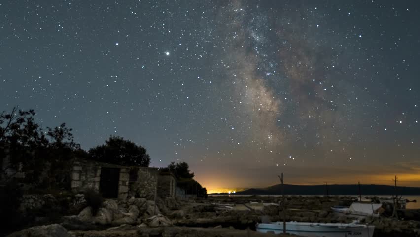 Milky way galaxy time lapse footage above old stone house and fishing boats on the rocky adriatic shore