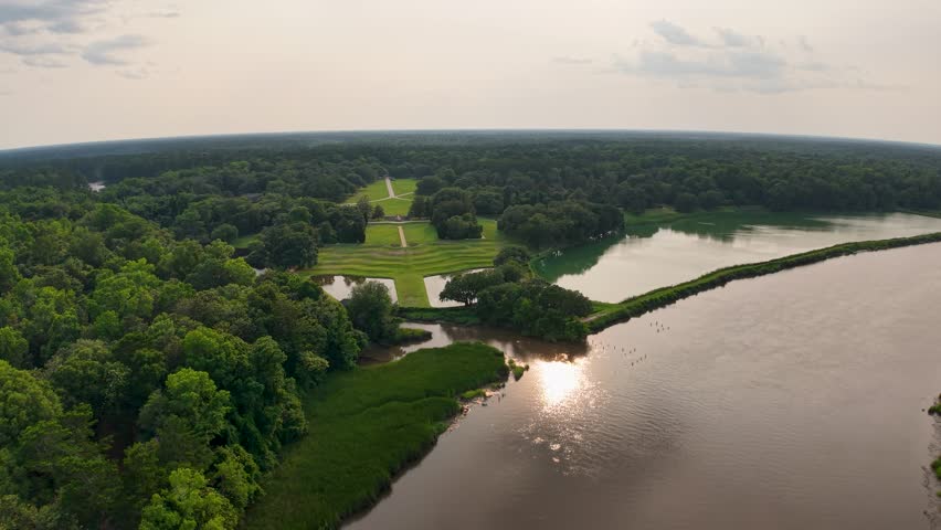 Drone footage of Middleton Place Plantation shows a wide river reflecting the sky and a long walkway along the banks with dense forests and lawns in Charleston, South Carolina.