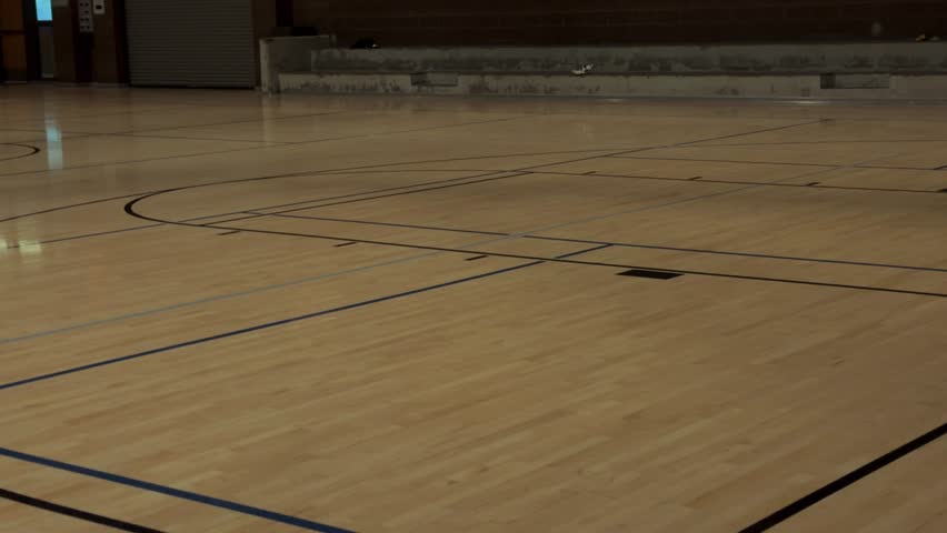 Slow right to left pan across empty indoor basketball court, ending behind wall for transition use