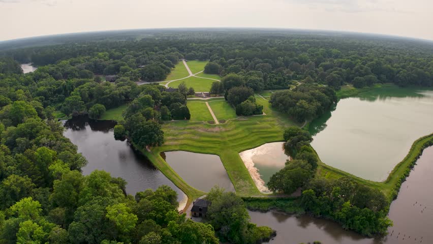 Drone footage captures a green rectangular field flanked by reflective ponds and surrounded by forest at Middleton Place Plantation near Charleston, South Carolina