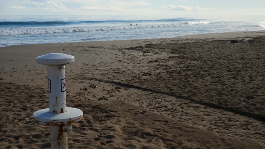 Rusted foot wash on the beach with surfers in the background. Slow motion x.05. Urbanova, Alicante, Spain.