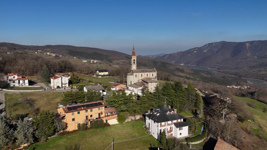 Aerial view of the historic Santi Salvatore e Gallo church situated in the picturesque Rabbini hamlet of Morfasso, Italy, surrounded by rolling hills and mountains