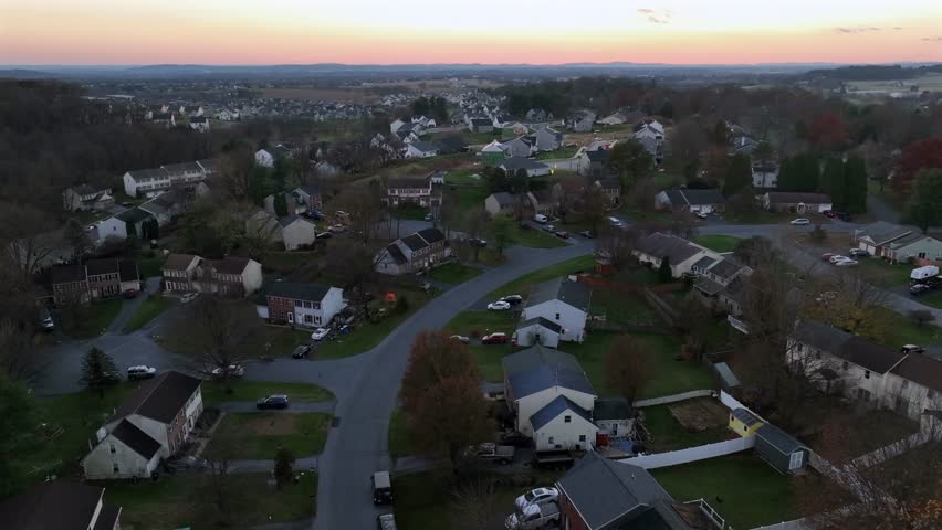 Residential area of american town in suburbia during sunset time. Aerial wide shot. Peaceful homes between colored trees in fall season. Single family houses in classic style architecture.