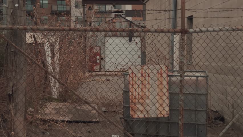 Slow steady zoom through chain link fence toward an abandoned industrial alley and loading area