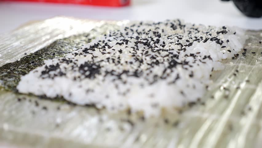 A gloved sushi chef sprinkles sesame seeds on rice while making sushi. Japanese cuisine, Asian cuisine close-up. Takeaways, food delivery.